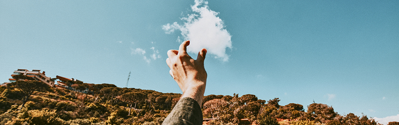 person reaches out to try and pinch the cloud in a blue sky-1280x400