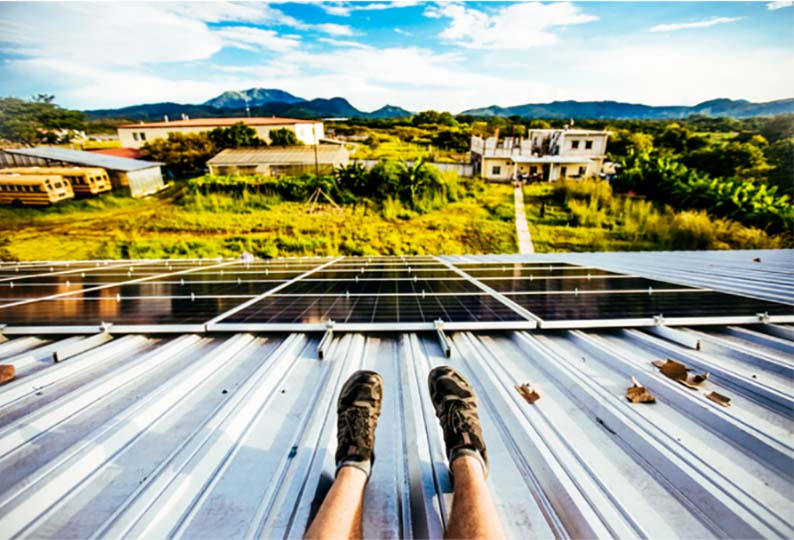 man sitting on rooftop with solar panel watching rural setting