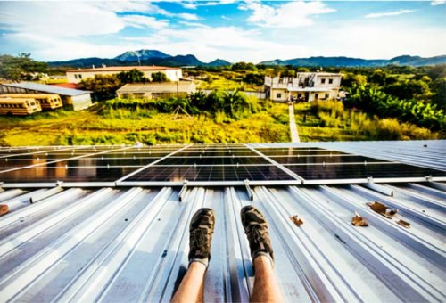 man sitting on rooftop with solar panel watching rural setting