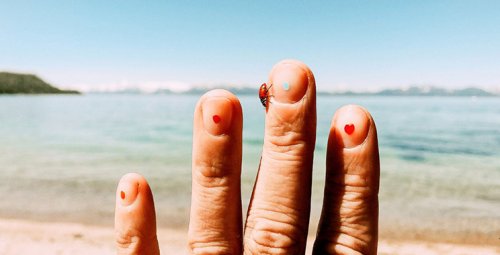 Close-up of a hand with a ladybug and drawn dots on the fingernails at the beach