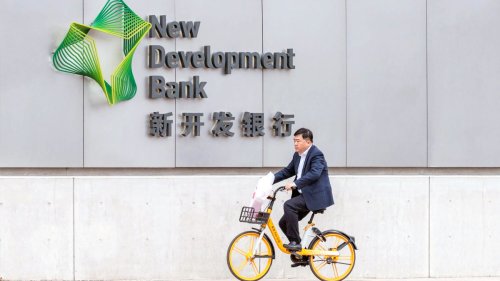 Chinese man riding on a bike past the New Development Bank logo on a wall